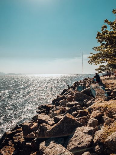 A vertical shot of a rocky beach and wavy sea under blue sky
