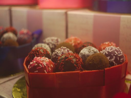 A closeup of Rum balls with colorful toppings in a heart-shaped box under the lights
