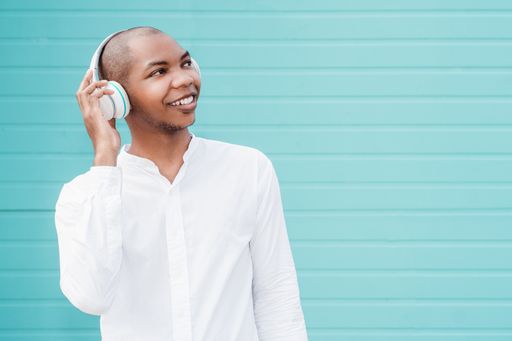 A cheerful Afro American with a white shirt and earphones posing at camera on a blue background