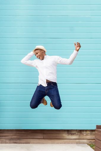 A vertical shot of cheerful Afro American in white hat jumping on a blue background