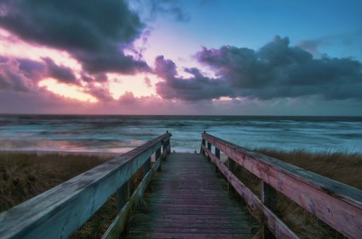 A long shot of a boardwalk leading to a beach with a colorful sunset in Wenningstedt, Sylt, Germany