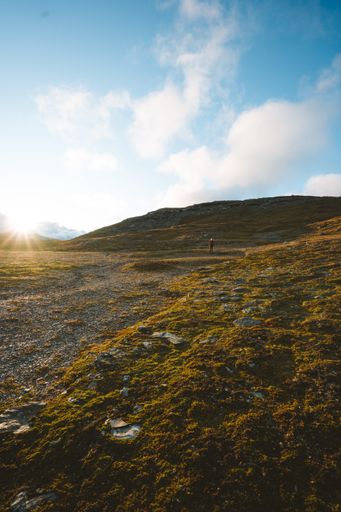 A beautiful scenery of green land surrounded by high rocky mountains with the bright sun in the background in Finse, Norway
