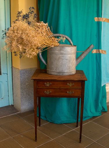 A vertical shot of a metallic watering can with some dry flowers on a wooden table