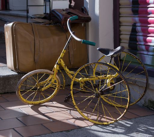 A closeup shot of an old and rusty bike near the suitcase in the street