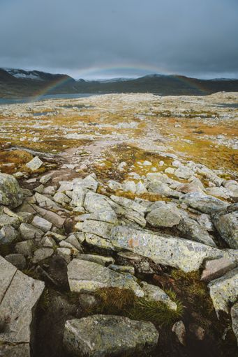 A vertical shot of land with a lot of rock formations and the rainbow in the background in Finse, Norway