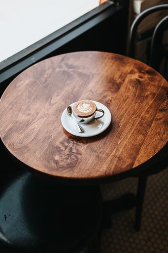 A very well made cappuccino in a cup with flower art on foam on a wooden round table