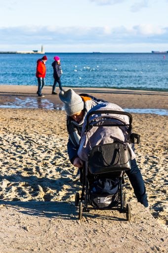 Adult woman adjusting a child buggy on a beach on a cold day at the seaside.