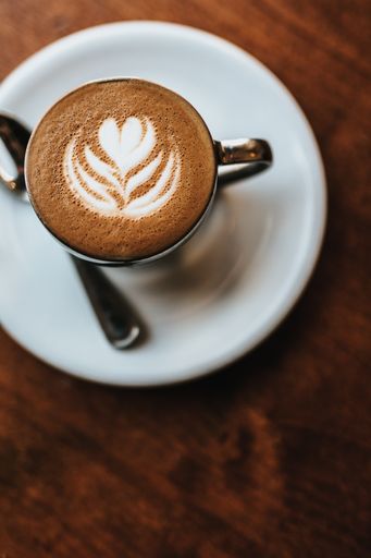 A beautifully made cappuccino served with flower art on the foam shot from an overhead view