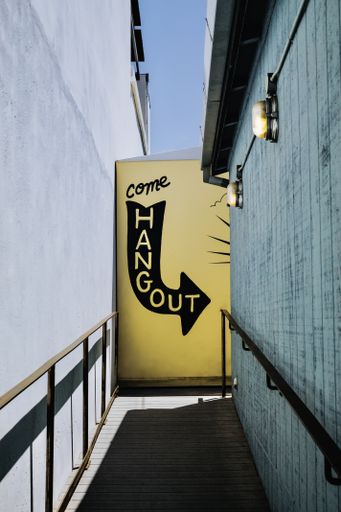 A narrow pathway with an arrow sign that reads "Come hangout" on an orange wall