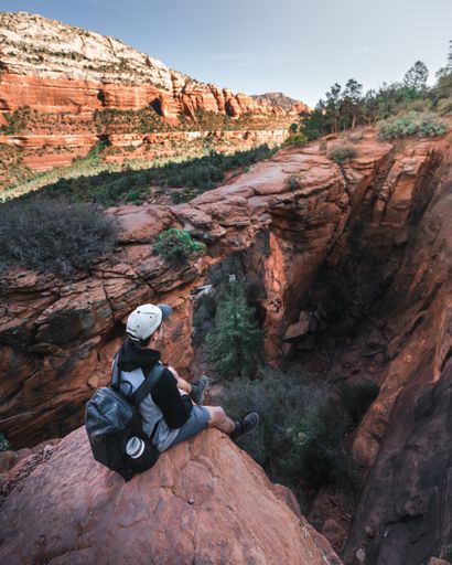 A high angle shot of a young hiker with a backpack resting on a cliff after reaching the top