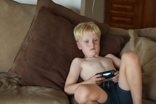 A young Caucasian boy playing video games at home on the sofa in soft afternoon light