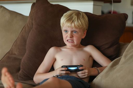 A young Caucasian boy playing video games at home on the sofa in soft afternoon light