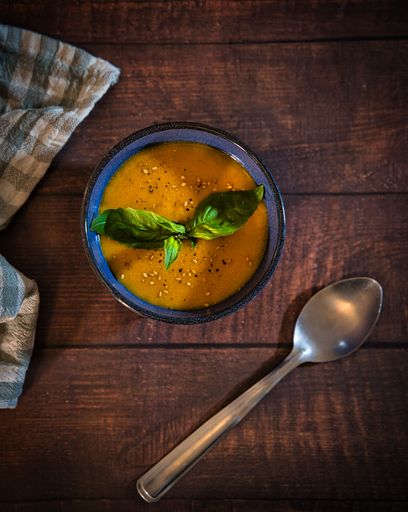 A vertical top view of a carrot cream soup with a decorated with basil and seeds on a wooden table