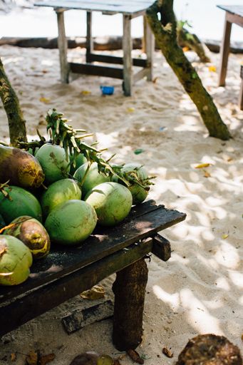 A vertical shot of some fresh coconuts on a wooden table in a beach