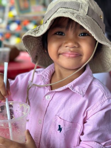 A vertical shot of a little girl wearing safari hat and pink blouse, drinking smoothie.