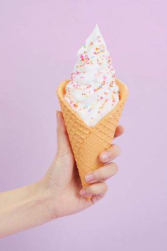 A female's hand holding delicious soft ice cream with sprinkles in a crispy waffle cone on a purple background