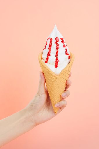 A female's hand holding delicious soft ice cream with topping in a crispy waffle cone on a pink background