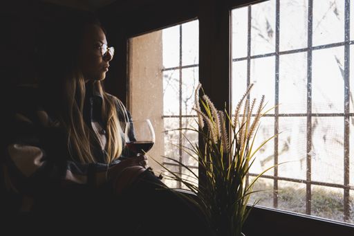 A young woman at home sitting near window relaxing in her living room reading a book and drinking tea