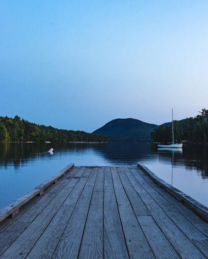 A vertical shot of a wooden pier leading into calm reflective lake water