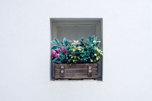 An isolated shot of a small windowsill with a wooden pot of artificial plants on a white wall