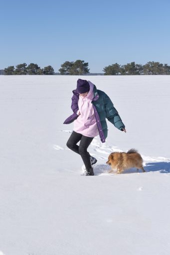 A shallow focus shot of a young female playing with her Pomeranian dog on a snow