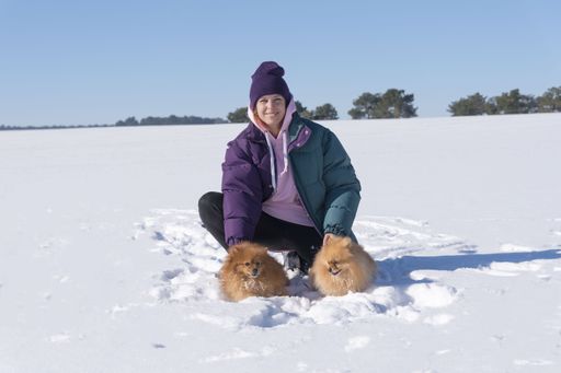 A shallow focus shot of a happy young female with two Pomeranian dogs on the snow