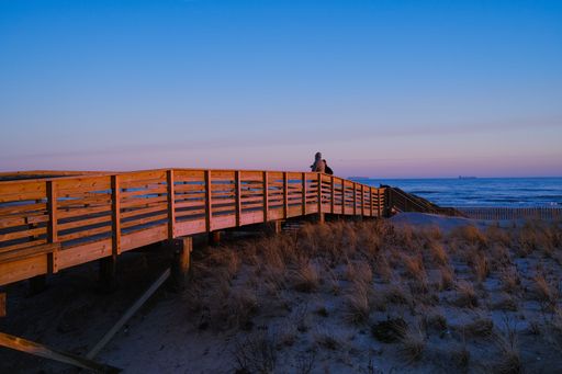 A closeup shot of two people on a wooden bridge over a sandy coast of an ocean during sunset