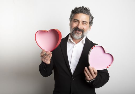 A happy bearded male in suit holding an empty red heart-shaped box on a white background