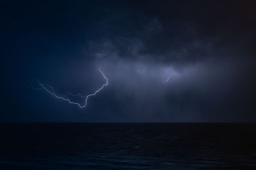A scenic view of lightning visible in the sky during a thunderstorm at night