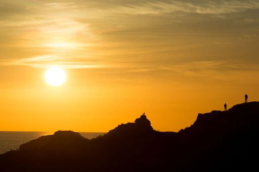 The people on massive rocks silhouetted against the backdrop of an orange sky at sunset.