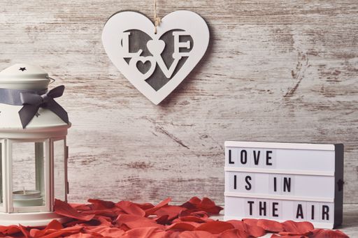 A heart-shaped frame, a lantern, and a board with a romantic text surrounded by rose petals
