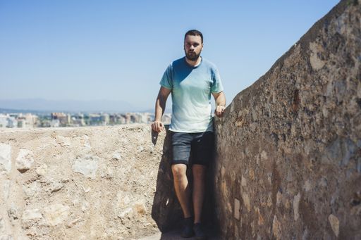 A nice shot of a handsome man standing near the stone wall