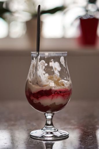 A vertical shot of a delicious half-empty dessert cup with a spoon on a reflective surface