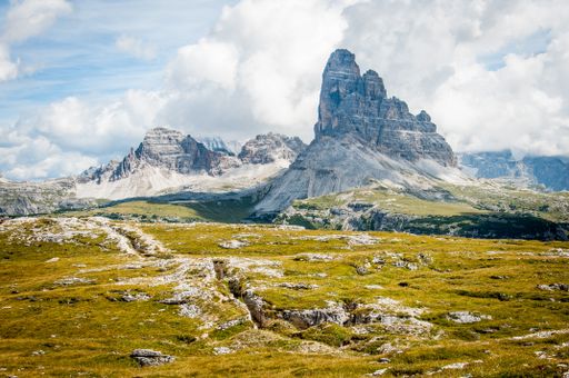 Tall Rock formation on wide field grass under cloudy blue sky during daytime