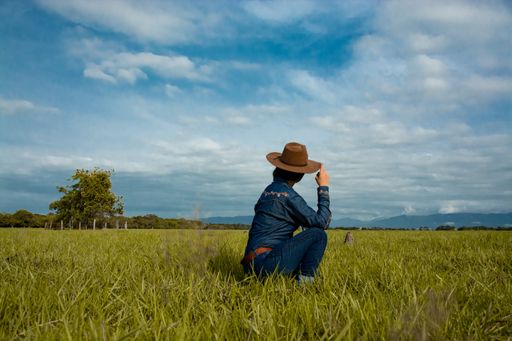 A shallow focus of a female dressed as a cowboy sitting on the ground in a field under a blue cloudy sky