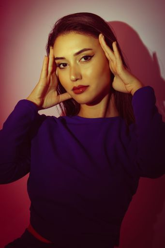 A young attractive Caucasian woman in a blue dress posing in a studio under a red light.