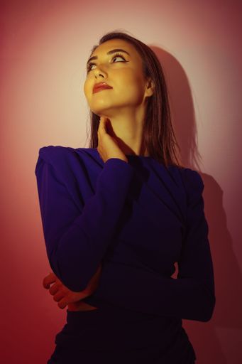 A young attractive Caucasian woman in a blue dress posing in a studio under a red light.