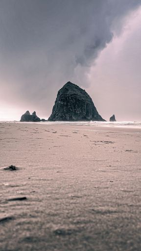 A vertical shot of a large rock formation in the sea waters seen through a sandy beach
