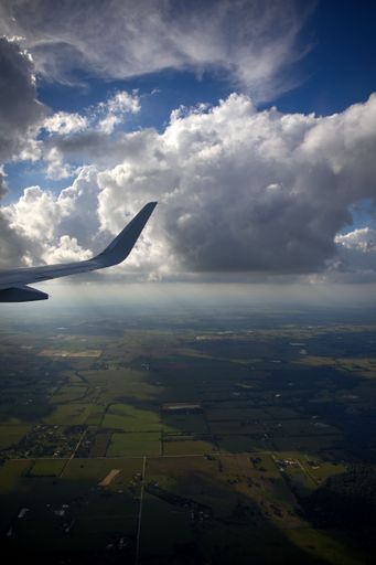 An aerial view of fields and clouds from the window of an aircraft.
