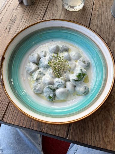 A top view of gnocchi with spinach in cheese sauce in blue and white plate on wooden table