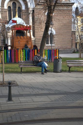 A man reading a newspaper on a bench near children park