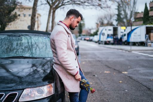 A fantastic shot of a handsome male standing near the car with a rose in his hands in the street