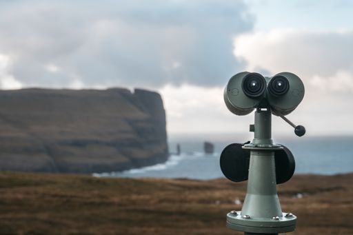 A closeup of a tower viewer on the ground surrounded by cliffs and the sea under a cloudy sky