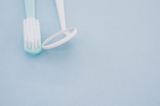 A closeup of a toothbrush and a dental mouth mirror on pastel blue background for a copy space