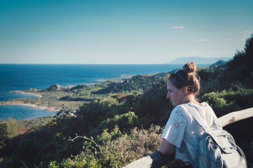 A shallow focus of a female wearing a shirt with a backpack and leaning on a fence while looking at the sea