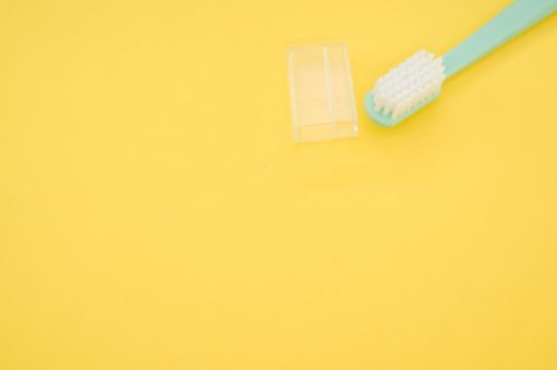 A turquoise toothbrush and a cap cover on a yellow surface for a copy space