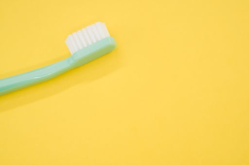 A turquoise toothbrush on a yellow surface for a copy space
