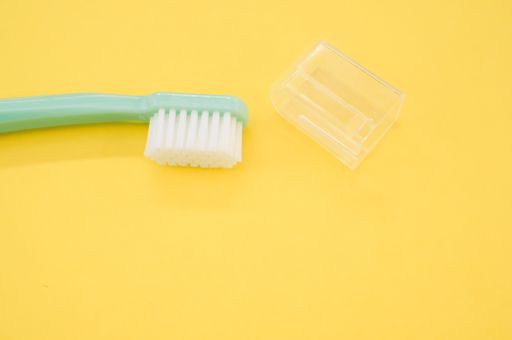 A turquoise toothbrush and a cap cover on a yellow surface for a copy space