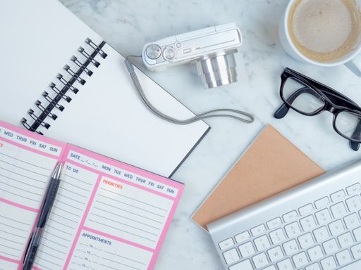 A top view closeup of the notebook, planner, eyeglasses, keyboard, coffee, and camera on the bed- concept planning a travel
