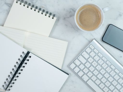 A top view closeup of the notebook, planner, coffee, smartphone, and keyboard on the table- conc